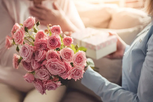Woman presenting a bouquet of pink roses with a gift box, representing thoughtful Mother’s Day flowers and the meaning of pink blooms