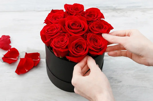 Close-up of hands gently touching soft rose petals in an open signature rose gift box, showing the texture and quality of fresh blooms